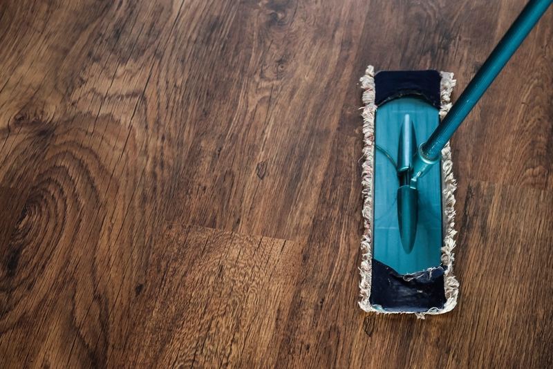 A flat microfiber mop with a teal handle on a hardwood floor, seen from above