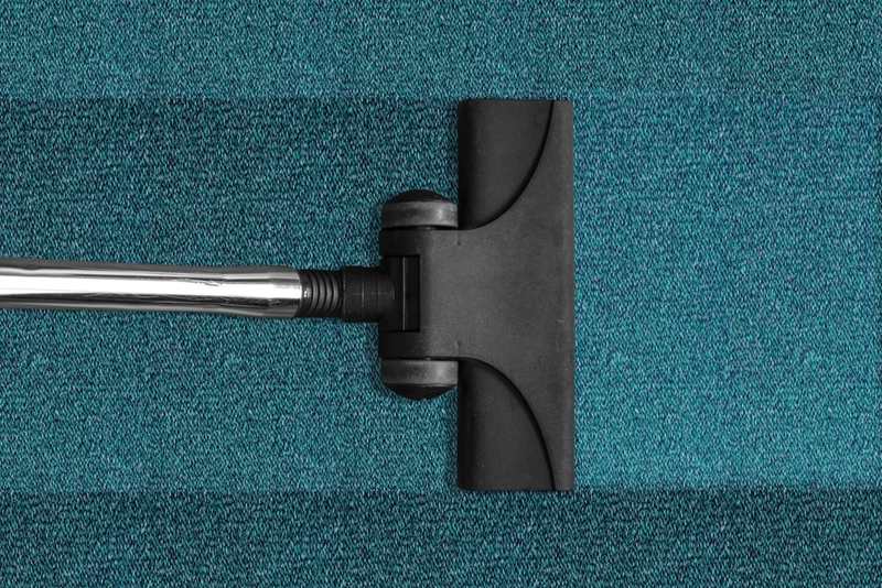 A vacuum cleaner head on a teal carpet with a clean stripe behind it